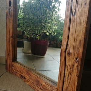 Puede incluir: Un espejo de madera r&uacute;stico con un acabado de madera natural. El espejo est&aacute; enmarcado con gruesas tablas de madera envejecidas. El espejo refleja una planta en maceta con hojas verdes y una maceta blanca.