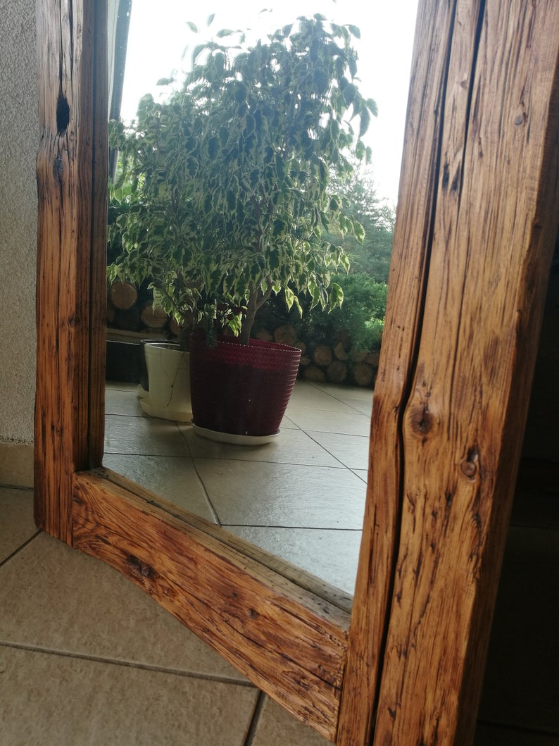 Puede incluir: Un espejo de madera r&uacute;stico con un acabado de madera natural. El espejo est&aacute; enmarcado con gruesas tablas de madera envejecidas. El espejo refleja una planta en maceta con hojas verdes y una maceta blanca.