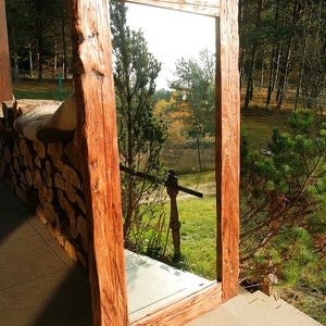 Puede incluir: Un espejo grande de madera r&uacute;stica con un marco rectangular. El marco est&aacute; hecho de madera gruesa y desgastada con un acabado marr&oacute;n natural. El espejo refleja una vista de &aacute;rboles y una zona de c&eacute;sped.