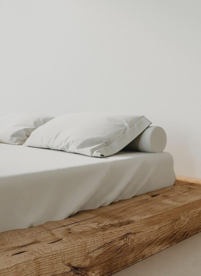 Puede incluir: Un juego de s&aacute;banas blancas que incluye una s&aacute;bana encimera, una funda de almohada rectangular y un coj&iacute;n cil&iacute;ndrico, todo sobre una base de cama de madera natural. La ropa de cama es de color blanco liso con una textura suave y mate.
