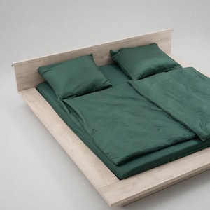Puede incluir: Una cama con estructura de madera clara y ropa de cama verde oscuro. El juego incluye una s&aacute;bana bajera, dos almohadas y un edred&oacute;n. La cama est&aacute; sobre un fondo blanco liso.