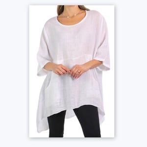May include: A white linen tunic top with a round neckline and three-quarter sleeves. The top features a front pocket and a slightly asymmetrical hemline. The model is wearing black leggings. The tunic is a loose, flowing style.