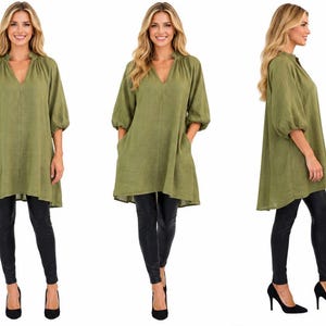 May include: An olive green tunic featuring a V-neckline, gathered collar detail, and three-quarter length puff sleeves with elasticized cuffs. The garment has a loose, flowing silhouette with side pockets, paired with black leggings and black heels.
