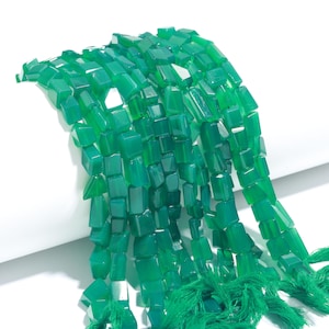May include: Strands of vibrant green gemstone beads. Each bead is a faceted cube, creating a textured surface. The beads are strung together, with green tassels at the ends. The gemstones have a polished, glossy finish.