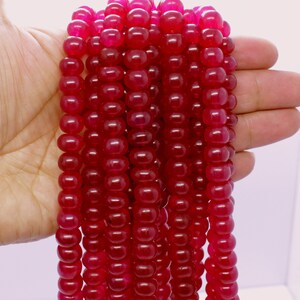 Puede incluir: Una hebra de cuentas de piedras preciosas de color rojo intenso. Las cuentas son redondas y lisas, y están enhebradas en un hilo transparente. Las cuentas tienen un diámetro aproximado de 10 mm.