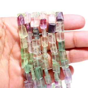 Puede incluir: Una hebra de cuentas de fluorita multicolores. Las cuentas son rectangulares y tienen una variedad de tonos de verde, morado y blanco.