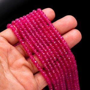 Könnte beinhalten: Stränge facettierter, leuchtend pinkfarbener Edelsteinperlen. Die Perlen sind klein und rund, mit mehreren Facetten, die das Licht einfangen. Die Perlen werden in einer Hand vor schwarzem Hintergrund gehalten.