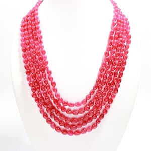May include: A multi-strand necklace made of pink oval-shaped beads. The necklace is layered and hangs to the chest.
