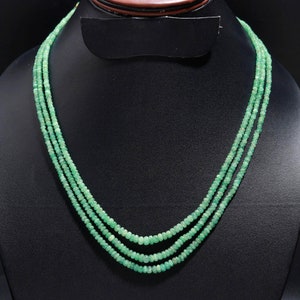 Peut inclure: Un collier à trois rangs composé de petites perles rondes vert clair. Le collier est présenté sur un présentoir à bijoux noir, mettant en valeur le design délicat et la couleur des perles de pierres précieuses.