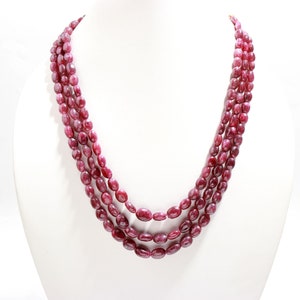 May include: A multi-strand necklace made of oval-shaped, deep red ruby beads.