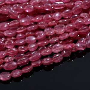 May include: A strand of pink oval-shaped gemstone beads. The beads are smooth and translucent, with a slight shimmer.