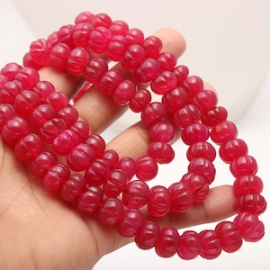 May include: A strand of bright pink, round, carved gemstone beads. The beads have a textured, ribbed surface.