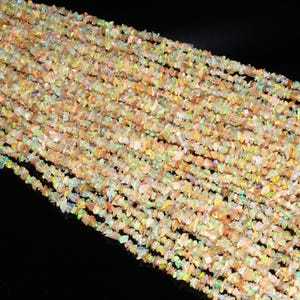 Puede incluir: Una hebra de cuentas de chip de ópalo iridiscente. Las cuentas son una mezcla de colores verde claro, amarillo y rosa. Las cuentas son pequeñas e irregulares en forma.