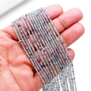 May include: A strand of light blue, green, and purple gemstone beads. The beads are small and round, and they are strung on a thin wire.