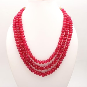 May include: A four-strand necklace made of bright pink beads. The beads are round and have a slightly textured surface.