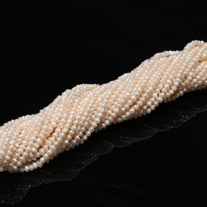 May include: A collection of small, creamy white pearls. The pearls are strung together, creating a thick, textured bundle. The pearls are on a white string, with a black background.