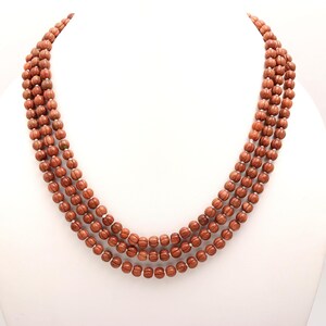 May include: A multi-strand necklace made of brown, round beads. The beads have a textured surface and are strung on a silver cord.