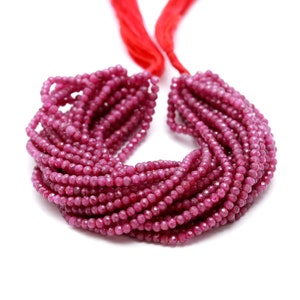 May include: A strand of ruby red faceted gemstone beads. The beads are small and round, and they are strung on a red cord.