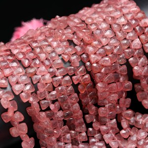 May include: A strand of pink rose quartz beads, each bead is faceted and has a square shape. The beads are strung together to create a long necklace or bracelet.