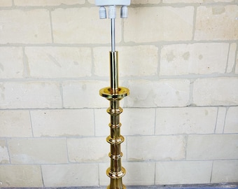 May include: A gold floor lamp with a white glass shade and three light bulbs. The lamp has a tall, slender base with a series of decorative rings.