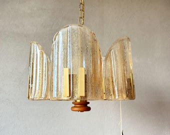 May include: A vintage-style chandelier with a gold chain and a textured, amber-colored glass shade. The shade has a unique, curved design with vertical lines and gold accents. The fixture includes wooden and gold metal components.
