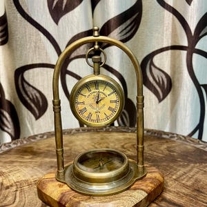 May include: A vintage brass desk clock and compass set. The clock face displays Roman numerals and the text "VICTORIA LONDON 1876". The compass is set into a wooden base, with a brass arch supporting the clock.