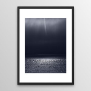 Könnte beinhalten: Ein Schwarzweißfoto eines dunklen, stürmischen Meeres mit einem einzigen Lichtstrahl, der durch die Wolken scheint.