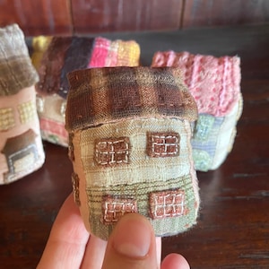 Könnte beinhalten: Vier kleine, handgefertigte Stoffhäuser mit verschiedenen Mustern und Farben. Die Häuser sind aus Patchwork-Stoff gefertigt und haben gestickte Details. Die Häuser stehen auf einer Holzoberfläche.