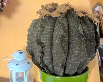 Puede incluir: Un cactus de tela marrón en una maceta verde. El cactus está hecho de tela y tiene un patrón a cuadros. La maceta es una maceta de cerámica verde simple.