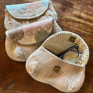 Könnte beinhalten: Drei gesteppte Stoffbeutel in Beige, Rosa und Braun. Die Beutel haben ein Patchwork-Design mit floralen Akzenten. Ein Beutel ist geöffnet und zeigt eine Brille. Die Beutel haben eine Vintage- und handgefertigte Ästhetik.