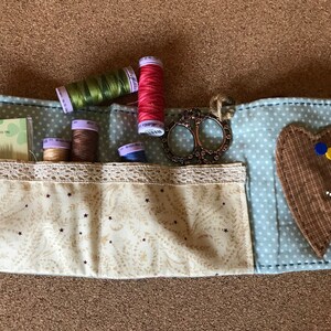 Puede incluir: Un kit de costura hecho a mano con carretes de hilo verde, rosa y marr&oacute;n. Incluye tijeras decorativas, agujas y un alfiletero en forma de coraz&oacute;n. La tela es azul claro con lunares blancos y un bolsillo estampado color crema. Medidas en cm.