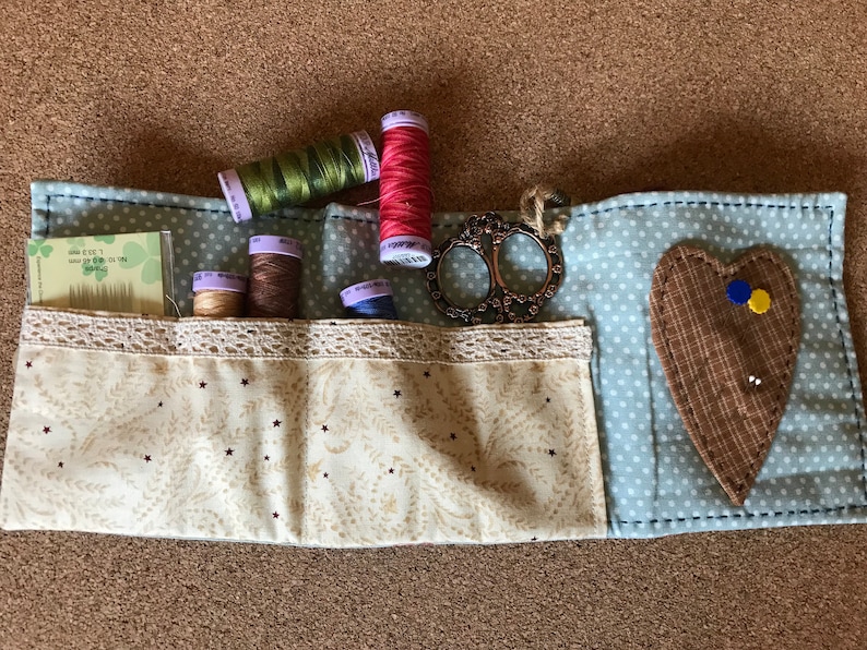 Puede incluir: Un kit de costura hecho a mano con carretes de hilo verde, rosa y marr&oacute;n. Incluye tijeras decorativas, agujas y un alfiletero en forma de coraz&oacute;n. La tela es azul claro con lunares blancos y un bolsillo estampado color crema. Medidas en cm.