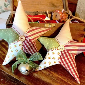 Può includere: Due stelle ornamentali in tessuto fatte a mano con un motivo a quadri rosso e bianco, un motivo a pois verde e bianco e un motivo floreale bianco. Le stelle sono decorate con un bottone bianco e un nastro verde e bianco.