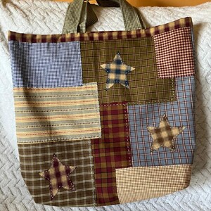 May include: A patchwork tote bag with a brown, green, blue, and red plaid pattern. The bag has three brown and tan stars sewn onto the front. The bag has a brown and white checkered handle.