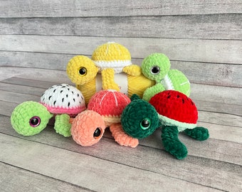 May include: Five crocheted turtle toys, each with a different fruit design. The turtles are green, pink, yellow, red, and white. They are all sitting on a wooden surface.