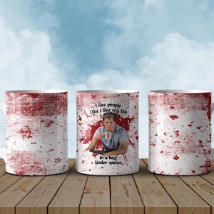 May include: White ceramic mug featuring a red splatter design and the text "I like people like I like my tea in a bag under water..." A man is pictured holding a mug. The mug is on a wooden surface with a blue sky background.