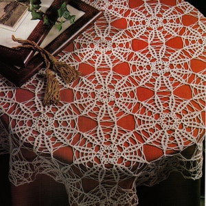 Puede incluir: Un mantel de ganchillo blanco con un delicado patrón floral, que presenta un diseño de estrella repetido. El mantel está colocado sobre una superficie roja.