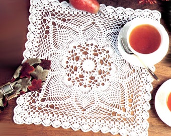 May include: White crocheted doily with a delicate, intricate design. The doily is square shaped and features a central motif with radiating patterns.