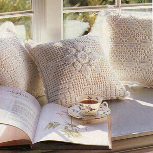 May include: A white crocheted pillow with a floral design sits on a windowsill with a book and a cup of tea. The book is open to a page with a botanical illustration and the text "VALERIAN".