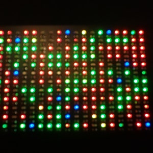 Puede incluir: Primer plano de una placa rectangular negra con una cuadrícula de luces rojas, verdes y azules. Las luces están dispuestas en un patrón, creando una pantalla colorida.