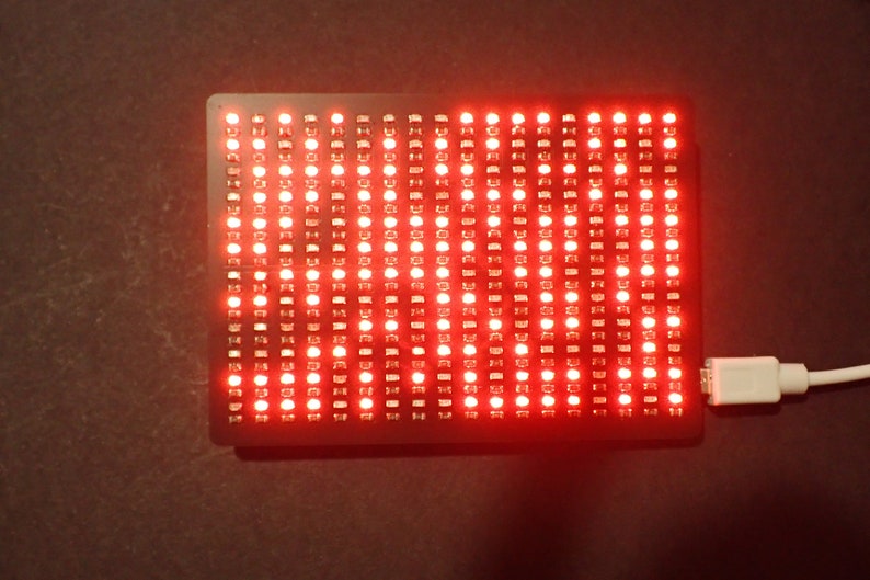K&ouml;nnte beinhalten: Ein rotes LED-Matrix-Display mit einem angeschlossenen USB-Kabel. Das Display befindet sich auf einer dunklen Oberfl&auml;che.