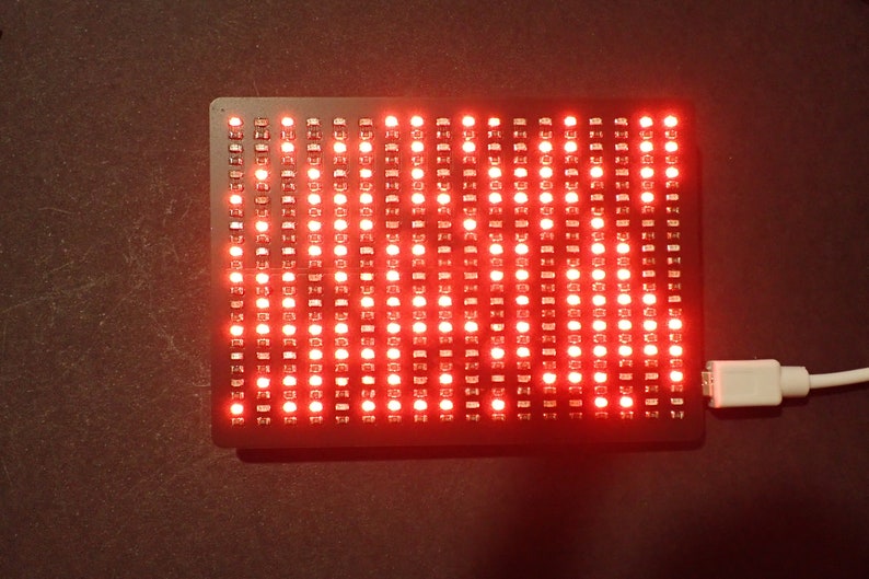 K&ouml;nnte beinhalten: Ein rotes LED-Matrix-Display mit einem angeschlossenen USB-Kabel. Das Display befindet sich auf einer dunklen Oberfl&auml;che.