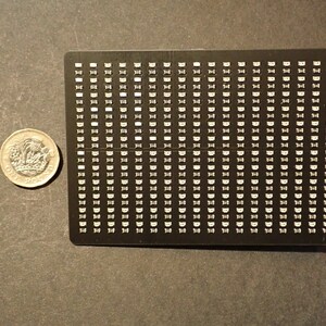 K&ouml;nnte beinhalten: Eine schwarze rechteckige Platte mit einem Raster aus kleinen wei&szlig;en Quadraten. Die Platte ist etwa so gro&szlig; wie ein 1-Euro-St&uuml;ck.