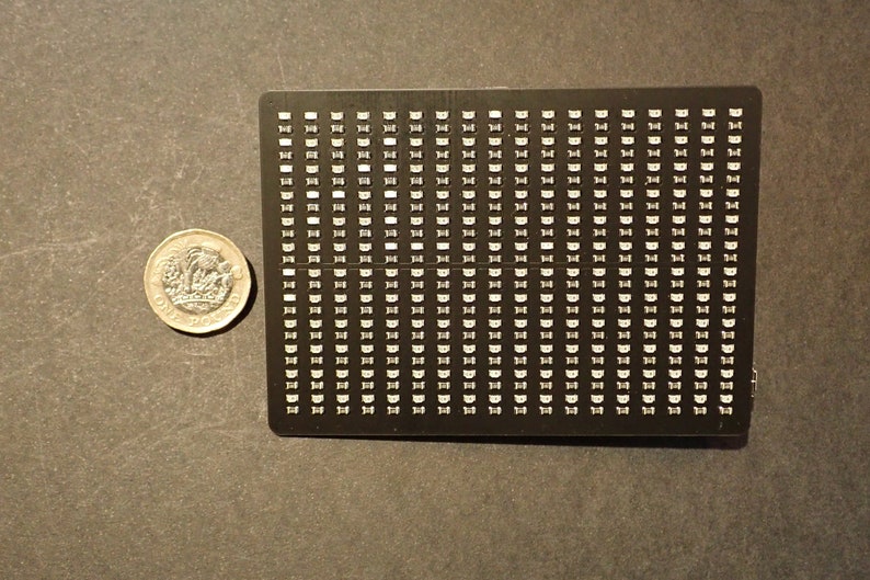 K&ouml;nnte beinhalten: Eine schwarze rechteckige Platte mit einem Raster aus kleinen wei&szlig;en Quadraten. Die Platte ist etwa so gro&szlig; wie ein 1-Euro-St&uuml;ck.