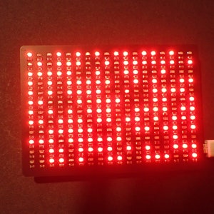 K&ouml;nnte beinhalten: Ein rotes LED-Matrix-Panel mit einem angeschlossenen USB-Kabel. Das Panel leuchtet in einem leuchtenden Rot.