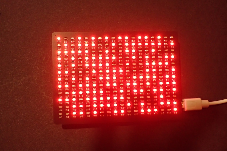 K&ouml;nnte beinhalten: Ein rotes LED-Matrix-Panel mit einem angeschlossenen USB-Kabel. Das Panel leuchtet in einem leuchtenden Rot.