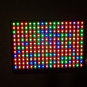 Puede incluir: Un panel LED rectangular negro con una cuadrícula de luces de colores. El panel está conectado a un cable USB blanco.