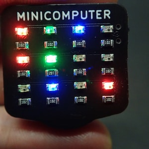 Peut inclure: Un appareil électronique noir avec l'inscription "MINICOMPUTER" et plusieurs lumières LED colorées. Les lumières sont rouges, vertes et bleues, disposées en rangées. De petits composants marqués "102" et "201" sont également visibles.