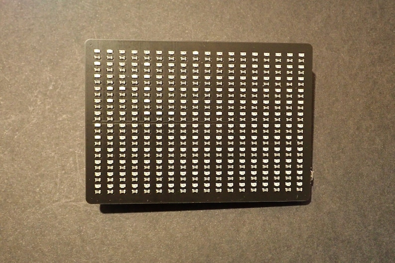 K&ouml;nnte beinhalten: Eine schwarze rechteckige Platine mit einem Raster aus kleinen wei&szlig;en Quadraten. Die Platine wird wahrscheinlich f&uuml;r Elektronikprojekte verwendet.