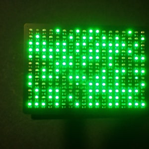 Può includere: Un display LED rettangolare con una cornice nera e una griglia di luci verdi. Il display è collegato a un cavo USB.